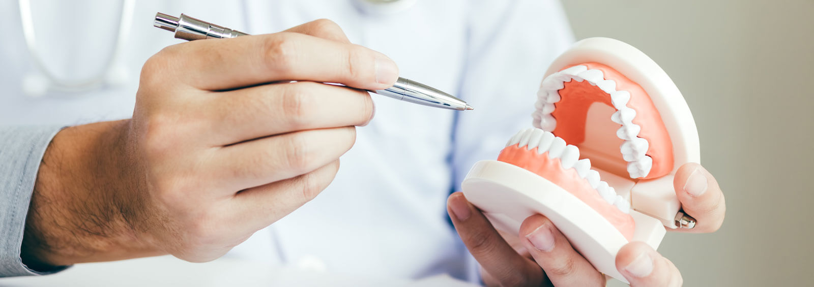 Asian Dentist Holding Pen Pointing To The Dentures And Is Descri